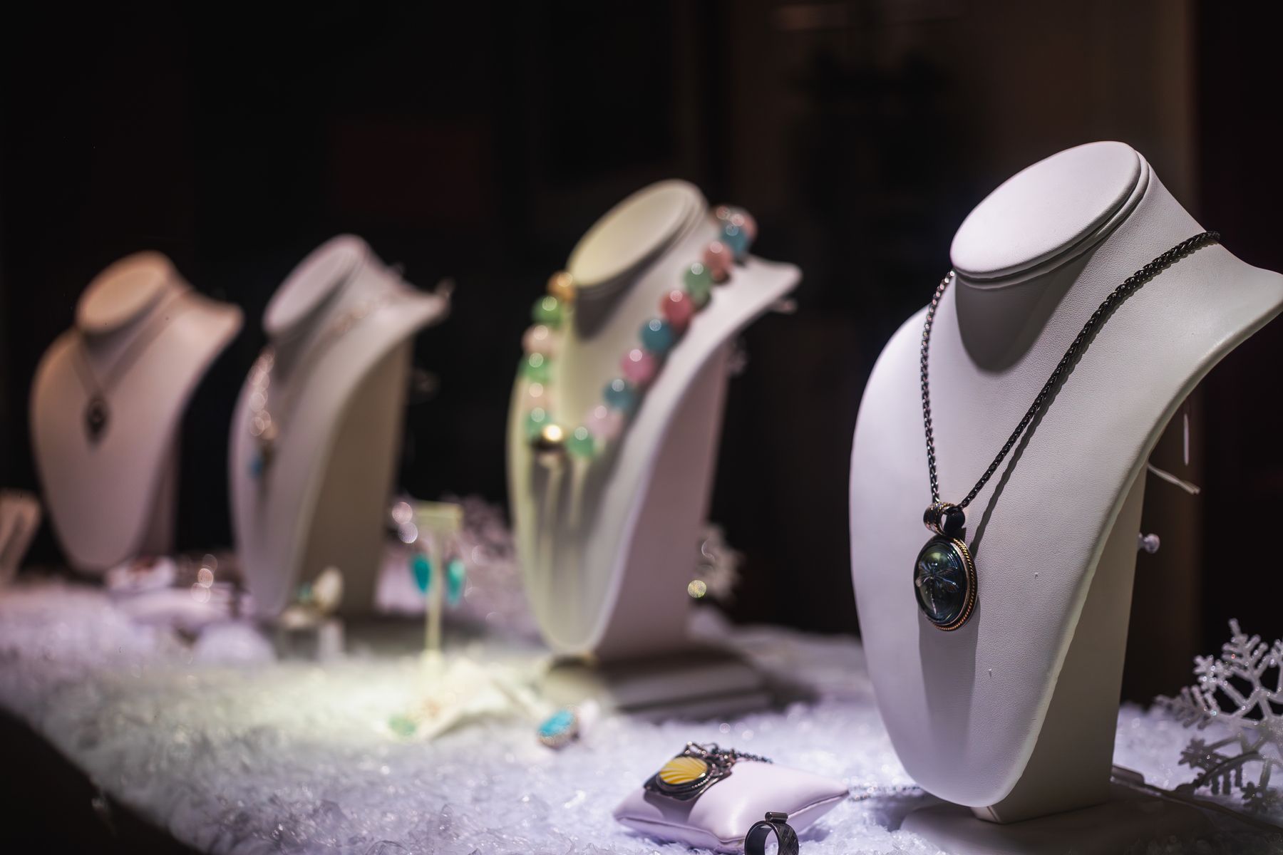 Necklaces displayed on jewelry busts under warm case lighting