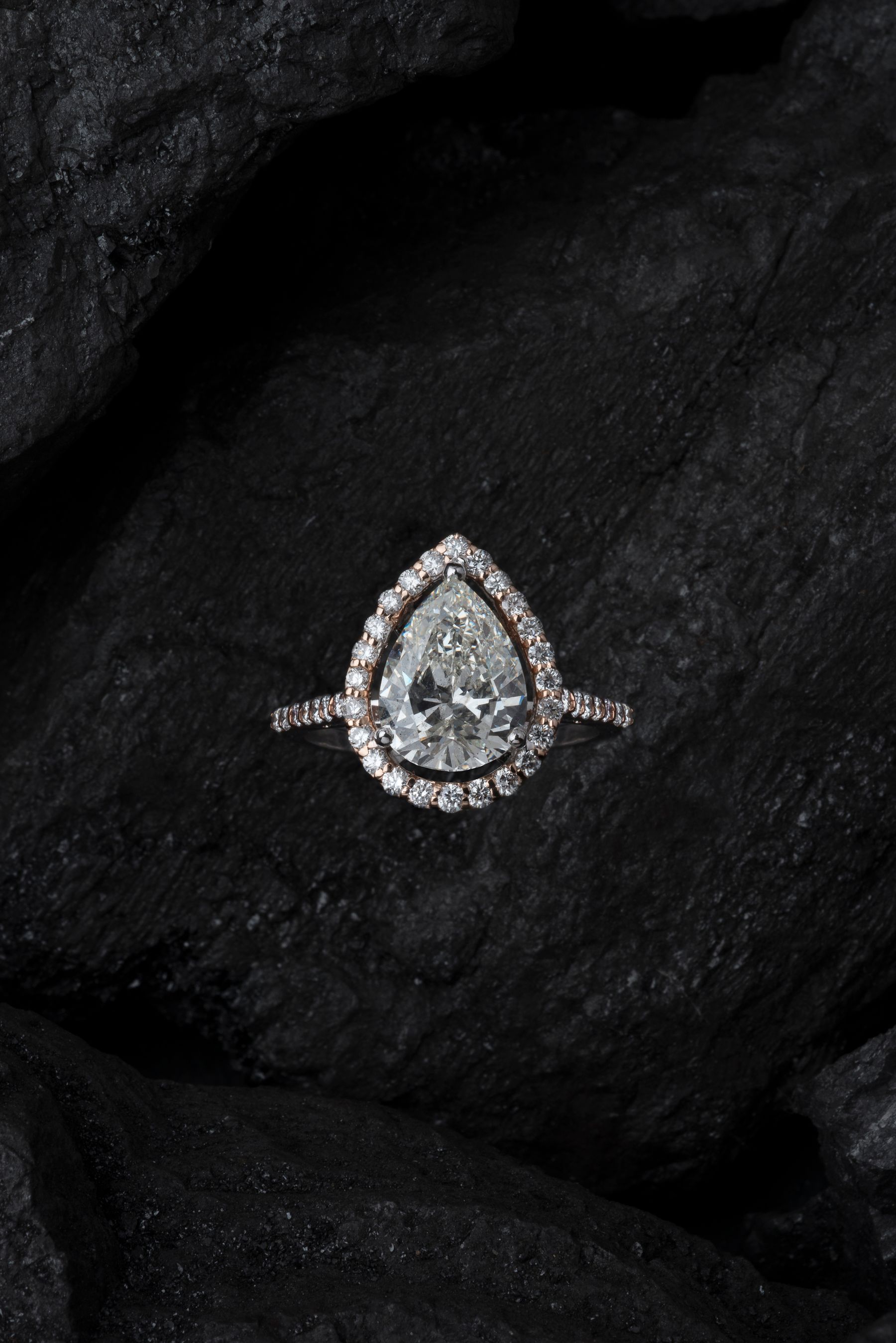 Pear-cut diamond halo ring resting on dark stone